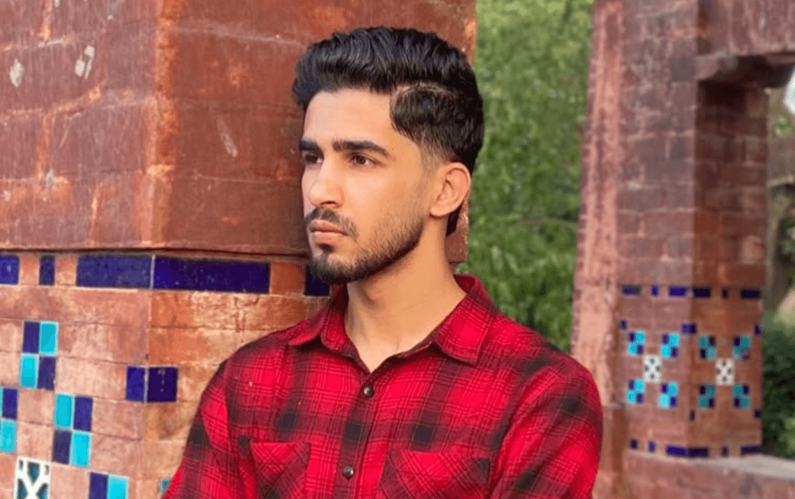 Portrait of Ahmed Javed with arms crossed, standing by a brick and tile pillar